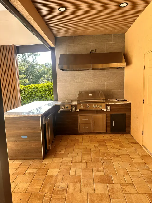 Finished outdoor kitchen with a built in grill under a wood plank ceiling